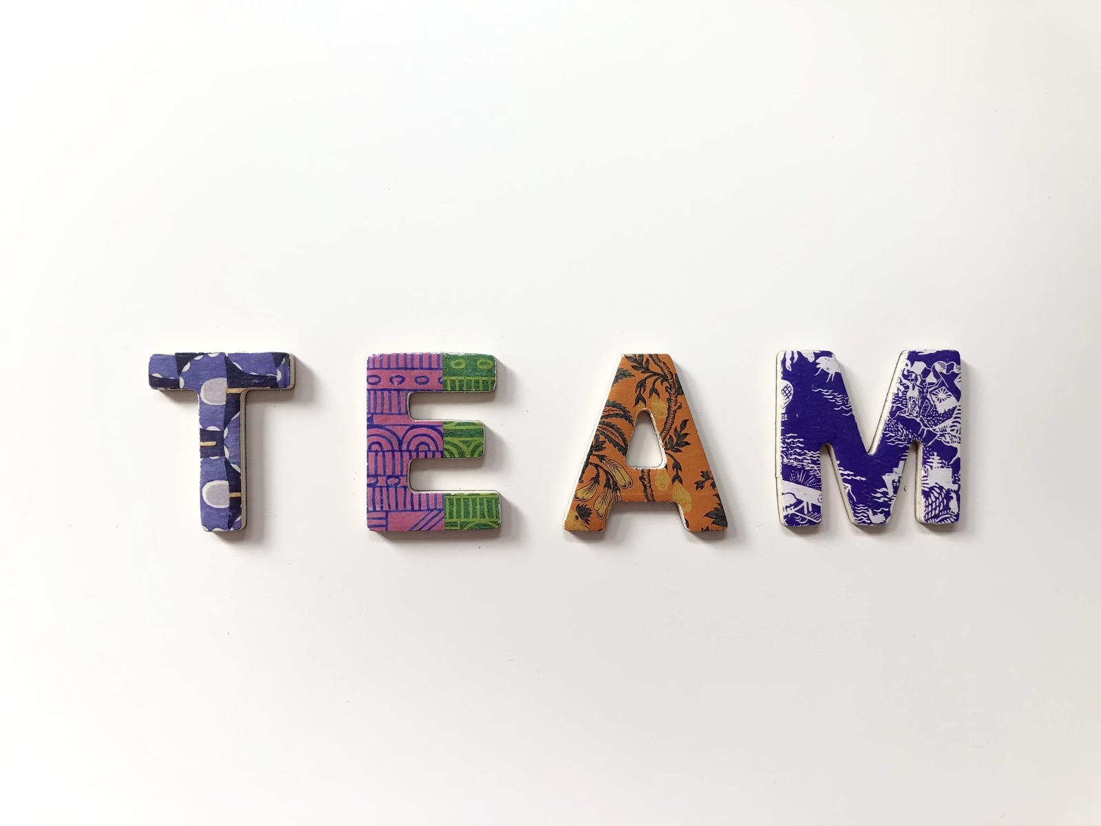 The word TEAM spelled out in four patterned wooden letters