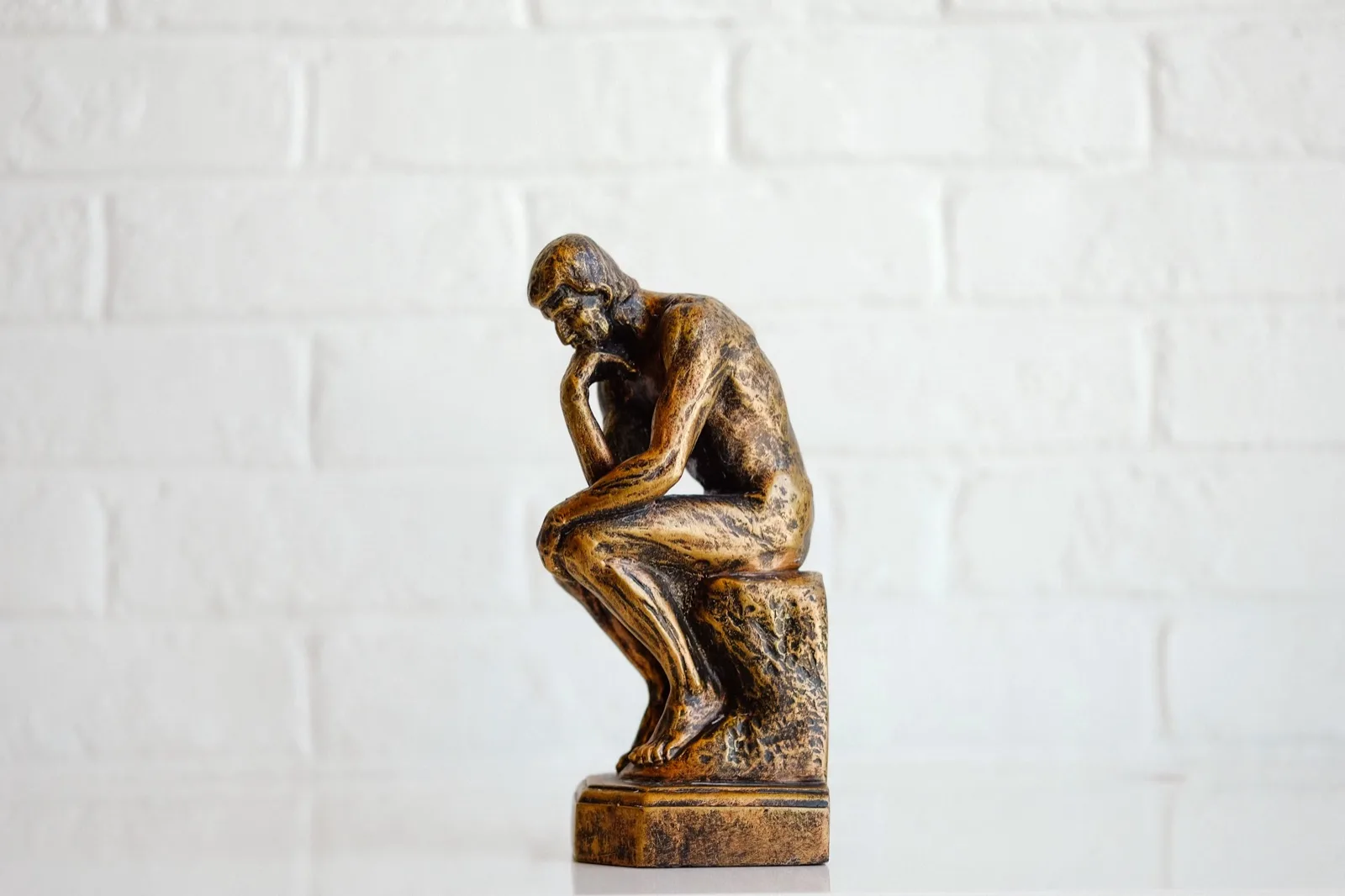 A small bronze Thinker figurine sitting against a white brick wall