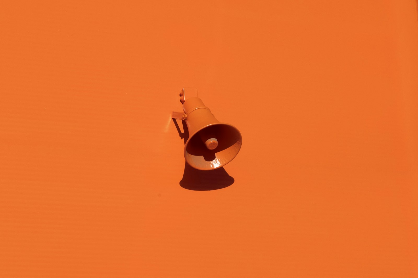 A white megaphone hanging against a flat orange wall